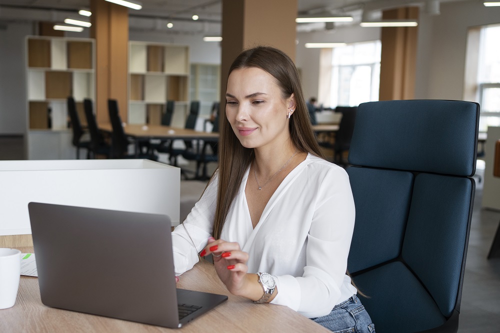 Na imagem há uma mulher de blusa branca, sentada em uma cadeira verde em frente a um notebook. A imagem representa a elaboração de um PDI.