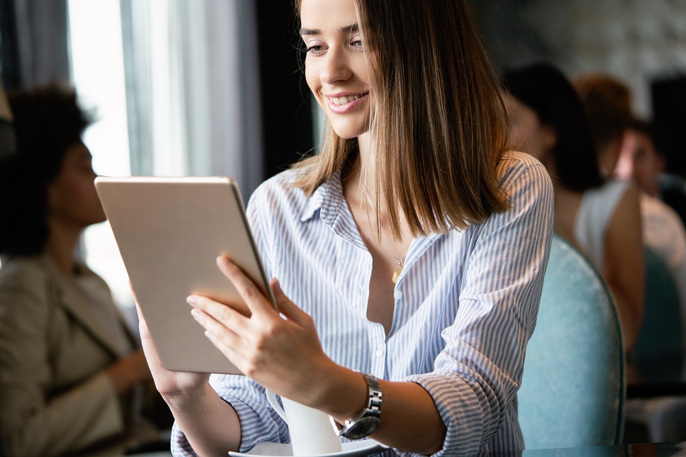 Na imagem há uma mulher sorrindo enquanto olhar para o seu tablet.