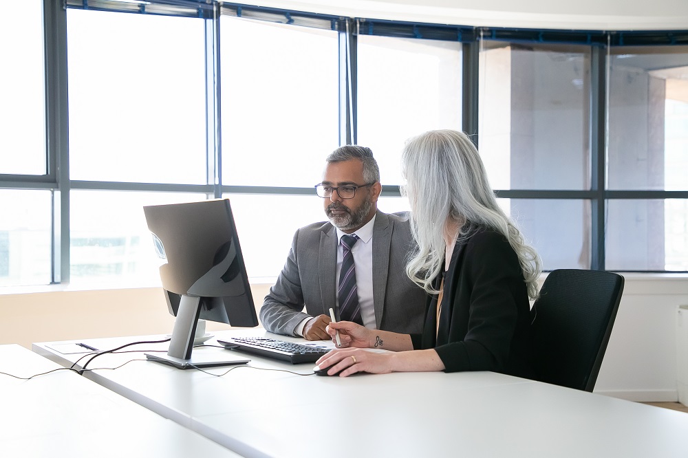 Um homem e uma mulher conversando em frente a um computador. A imagem representa a apresentação de objetivo SMART