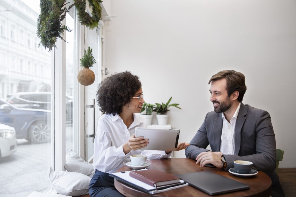 um homem e uma mulher estão sentados em uma mesa, aparentemente uma reunião, onde estão conversando e alinhando a avaliação de desempenho.