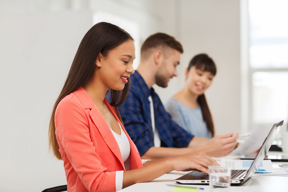  Colaboradores em um escritório, com foco em uma mulher digitando em um notebook.