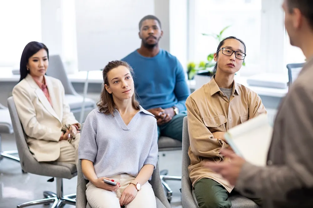 Equipe reunida em uma sala, estão olhando atentamente para um homem a sua frente que está aplicando um dos tipos de feedback.