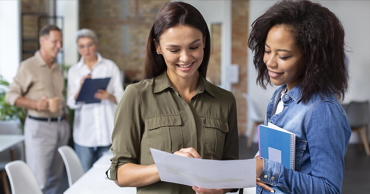 Duas profissionais em ambiente de escritório discutindo um gráfico em papel, representando a diferença entre cargo e função no trabalho.