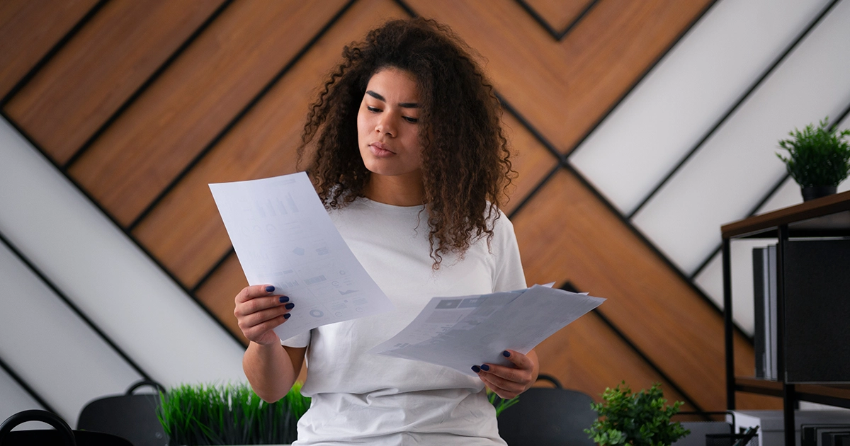 Mulher com cabelo cacheado analisa papéis em um escritório com expressão de dúvida, ilustrando por que o PDI não funciona devido a erros de estrutura.