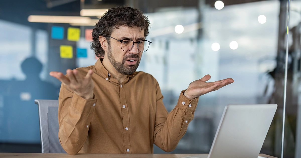 Homem com expressão confusa e mãos abertas olhando para a tela de um notebook no escritório, ilustrando o sentimento de frustração com erros comuns na aplicação do 9 Box