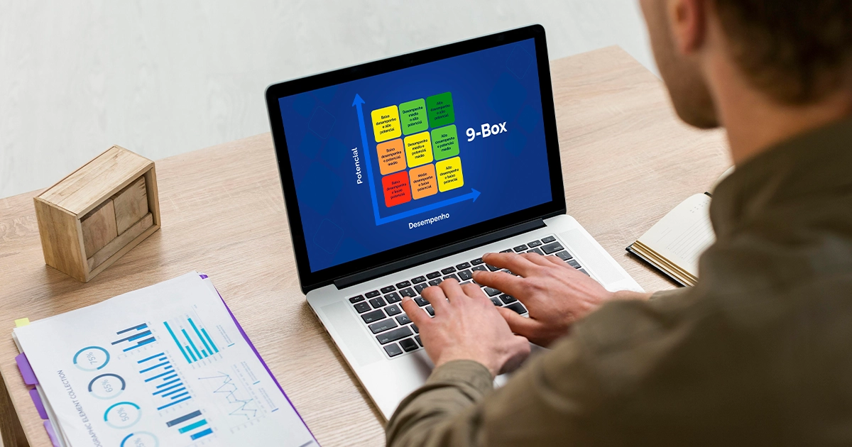 Homem trabalhando em um notebook que exibe na tela um gráfico de matriz 9-Box colorida com eixos de potencial e desempenho, ideal para entender o que fazer com cada quadrante 9 box.