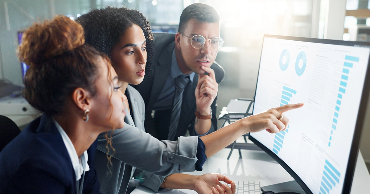 Três profissionais analisando relatórios em um software de gestão de treinamentos.