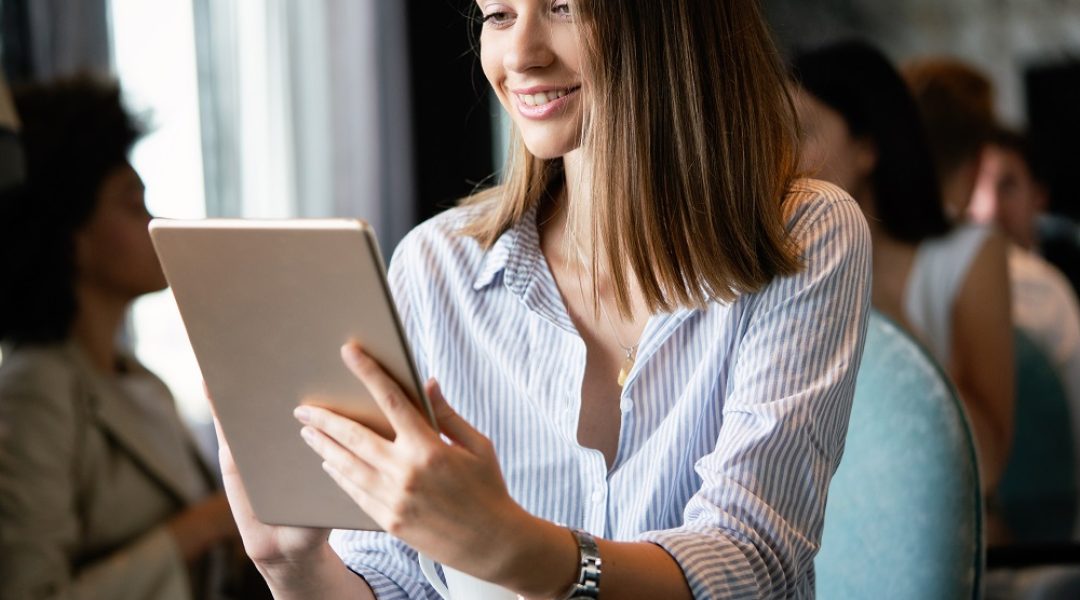 Na imagem há uma mulher sorrindo enquanto olhar para o seu tablet.