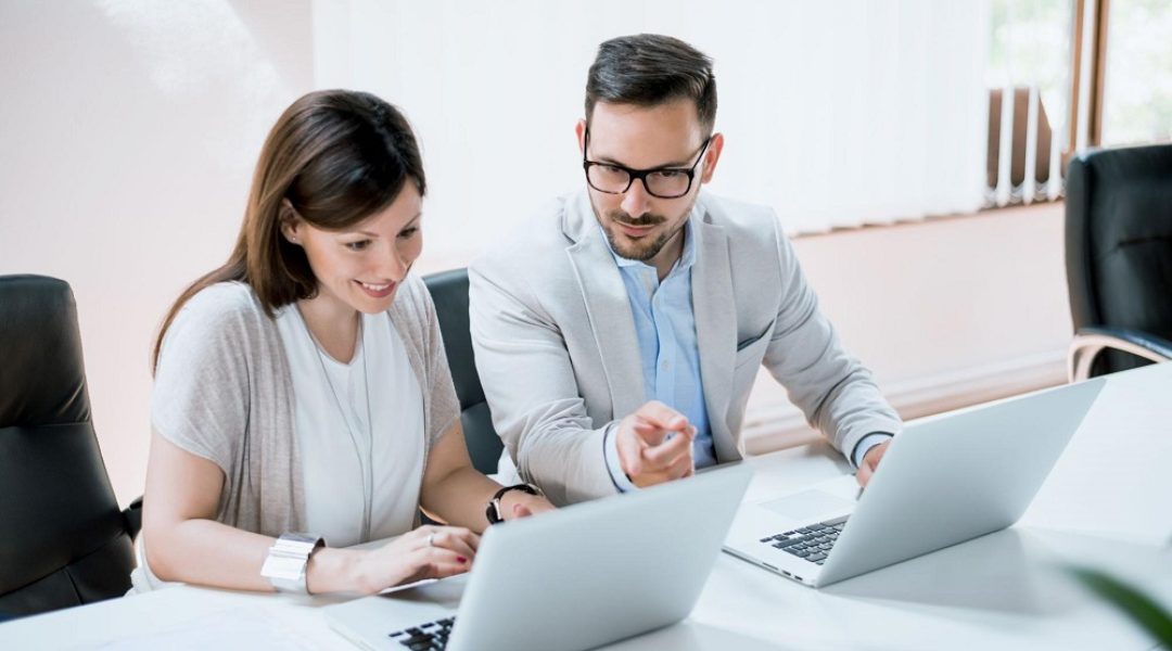 Um homem e uma mulher estão em uma sala, cada um está com um notebook. A imagem representa o onboarding através da plataforma LMS.