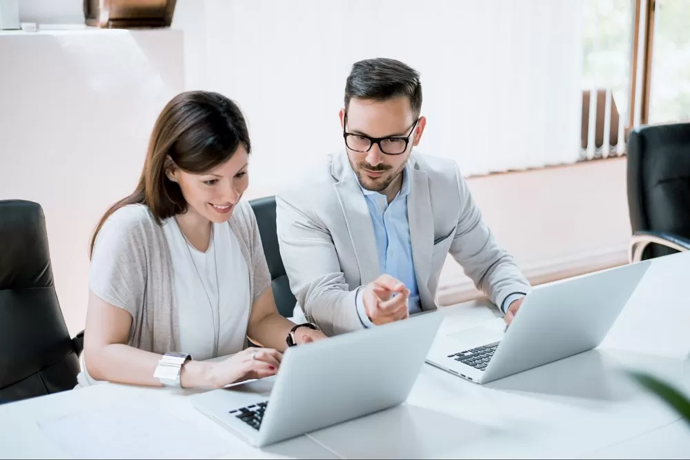 Um homem e uma mulher estão em uma sala, cada um está com um notebook. A imagem representa o onboarding através da plataforma LMS.